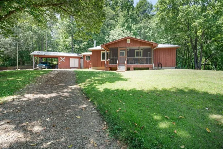 Ranch-style residence featuring a gravel driveway, an expansive lawn, and mature trees