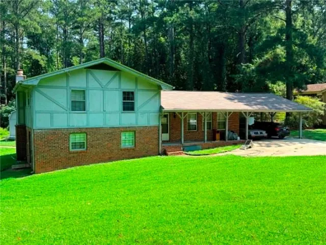 Expansive lawn leading to a brick and siding exterior, featuring a covered carport and mature trees