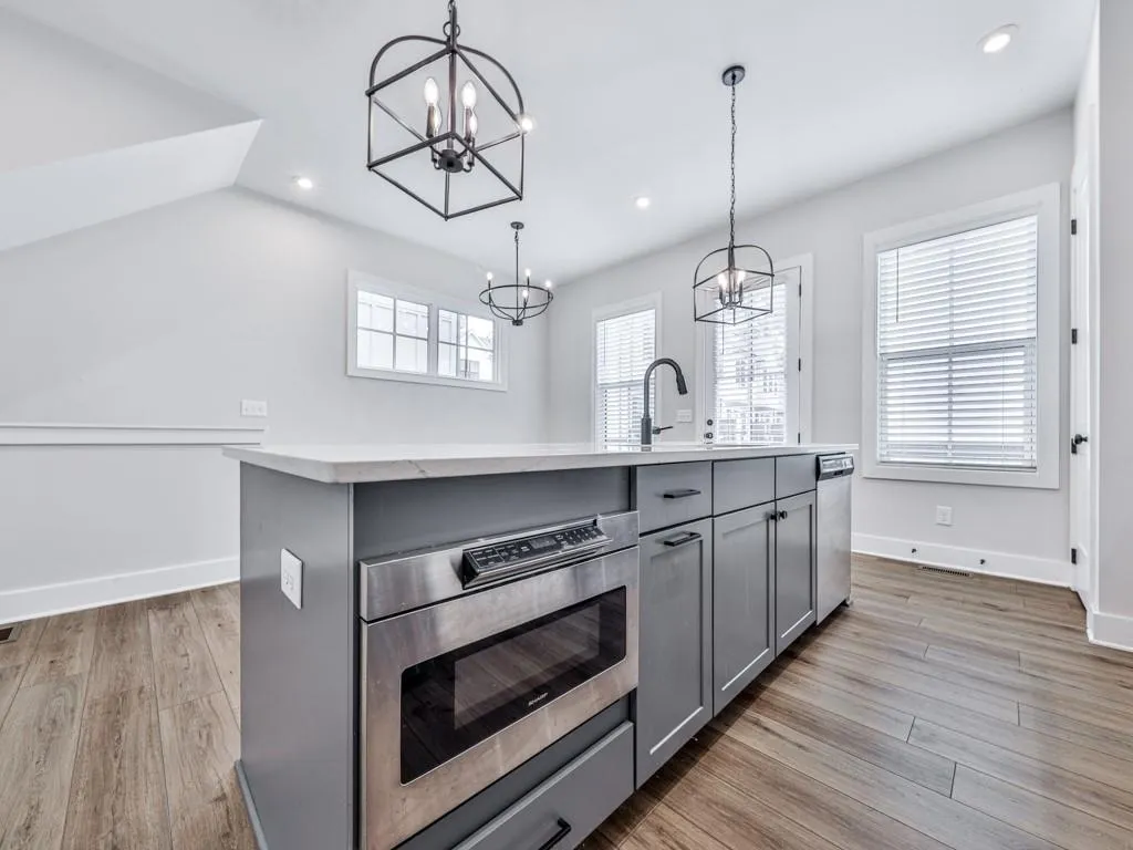 Kitchen with white cabinetry, light wood-type flooring, oven, pendant lighting, and an island with sink