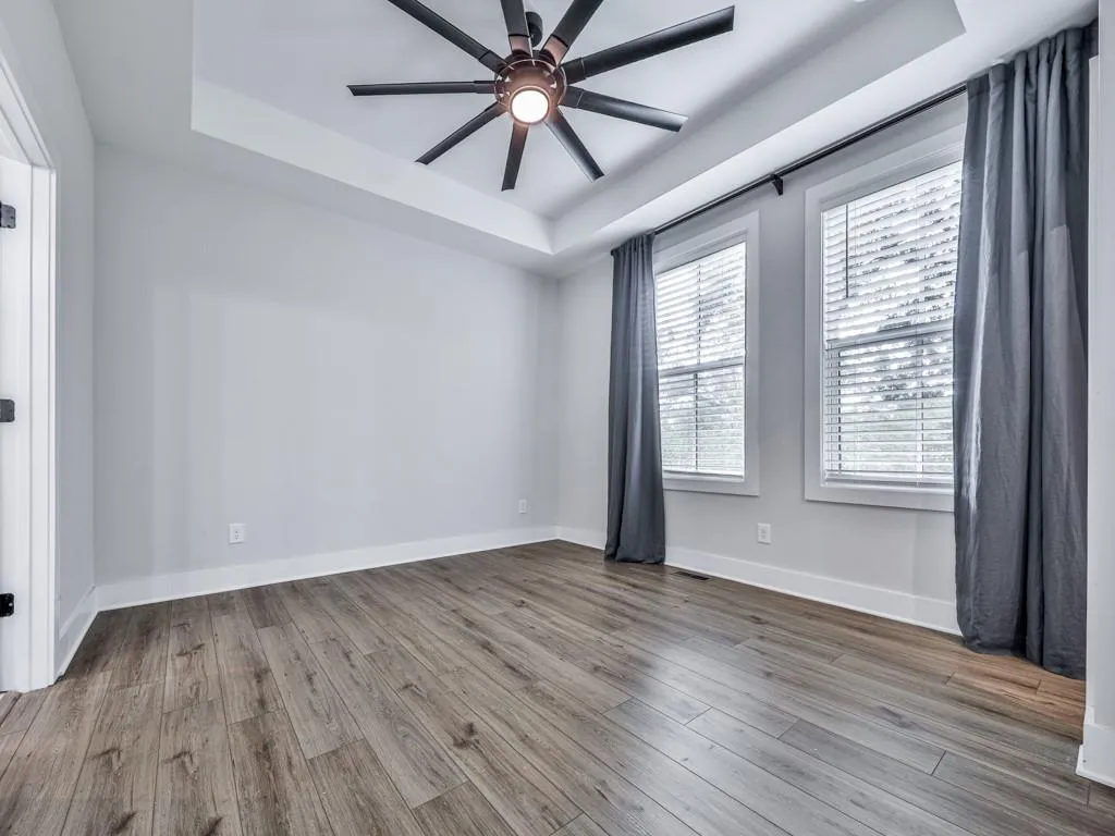 Unfurnished room featuring a tray ceiling, wood-style floors, and ceiling fan
