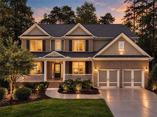 Brick and siding exterior featuring gabled rooflines, a covered front porch with white columns, a concrete walkway, and a concrete driveway leading to a two-car garage