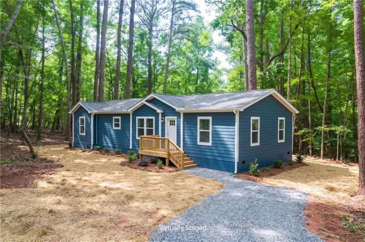 Blue siding exterior with white window trim, light-colored front door, and a natural wood deck