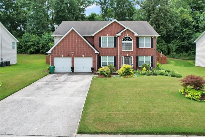 Two-story brick facade residence featuring a two-car garage, arched entry window, and established landscaping