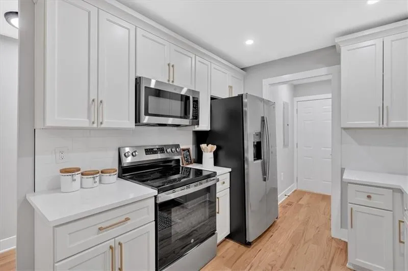 Kitchen with appliances with stainless steel finishes, light wood-type flooring, white cabinets, decorative backsplash, and recessed lighting