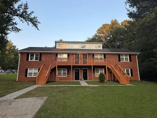 Brick facade with a dormer window, featuring exterior wooden staircases, a ground-level walkway, and landscaped grounds