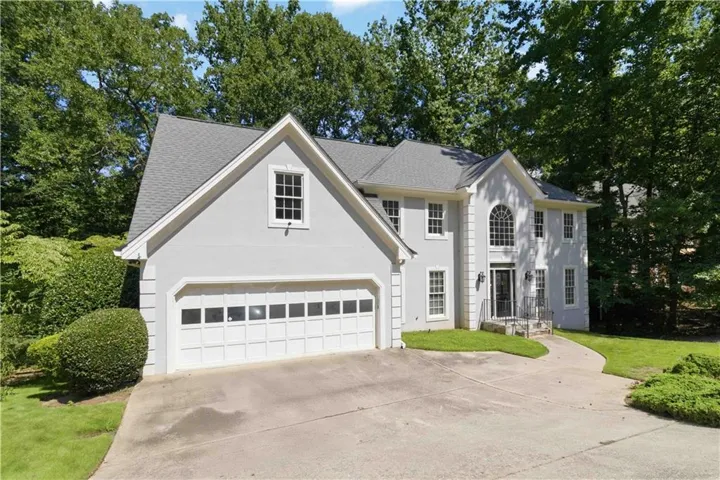 Two-story residence with a light-toned exterior, an attached two-car garage, and a curved concrete driveway