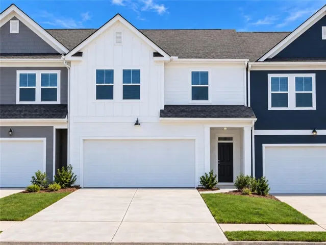 Modern townhome exterior featuring white vertical siding, a two-car garage, black front door, and a covered entry
