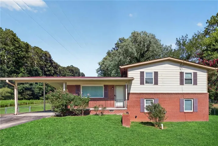 Split-level residence featuring a brick and siding exterior, front lawn, carport, and mature trees surrounding the property