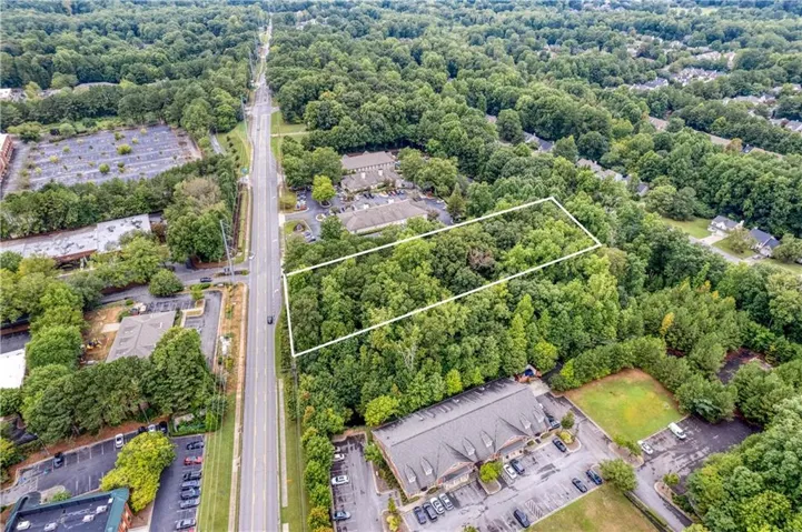 Expansive, tree-covered parcel outlined in white, bordered by a multi-lane road and commercial properties