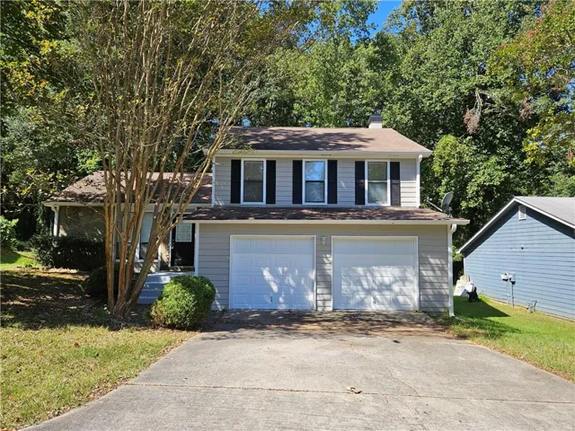 Two-story exterior with light-colored siding, contrasting dark shutters, and a two-car garage