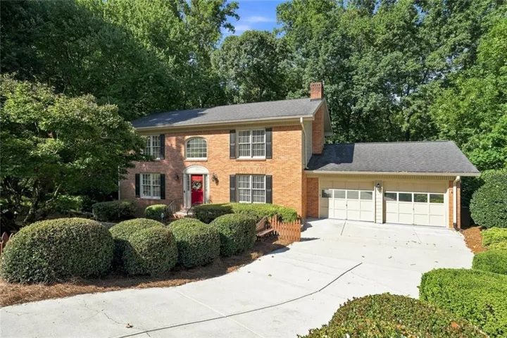 Brick exterior residence with a dual-car garage, mature landscaping, and a red entry door