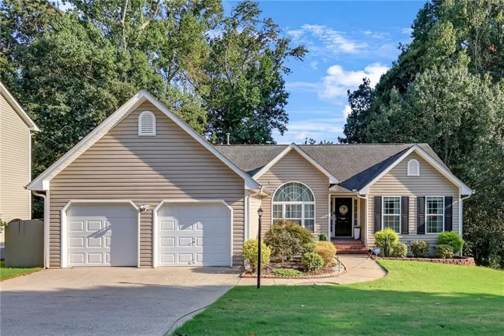 Siding exterior with a two-car garage, mature landscaping, arched window, and a paved driveway