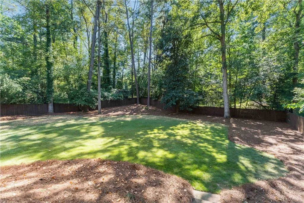 Expansive backyard featuring a lush lawn, mature trees, and a perimeter privacy fence