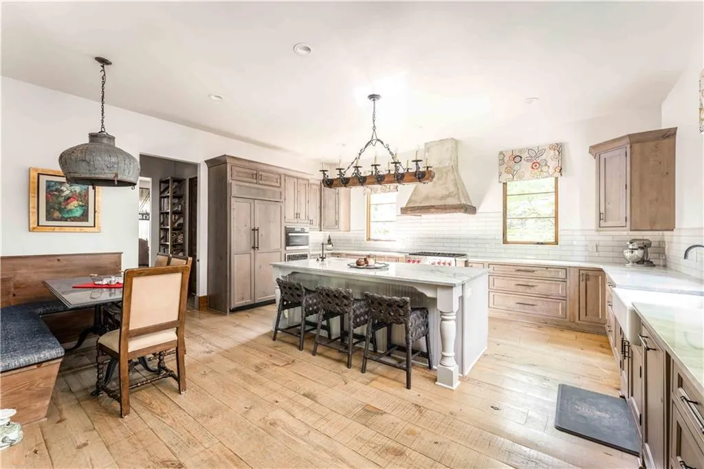 Spacious kitchen featuring light wood-finish flooring, a central island with seating, integrated appliances, a farmhouse sink, and subway tile backsplash