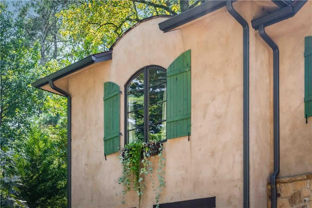 Stucco exterior featuring an arched window with dark framing and green wooden shutters