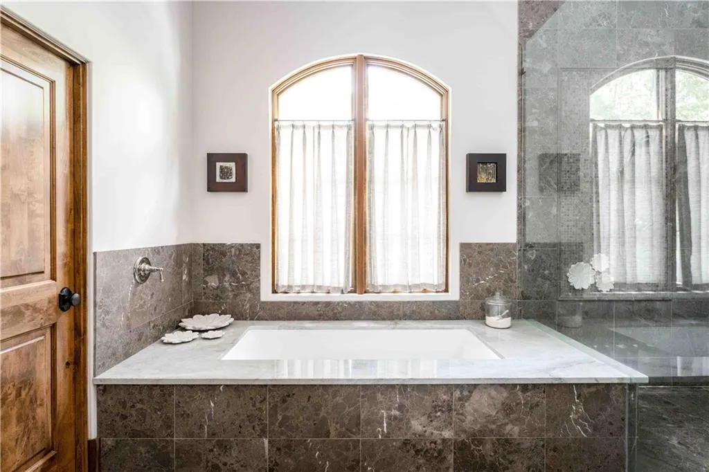 Built-in soaking tub featuring a light stone surround and dark tiled base