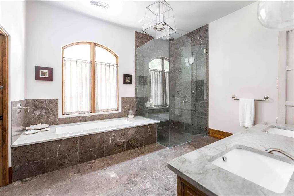Spacious bathroom featuring a built-in soaking tub, an arched window, and a glass-enclosed shower