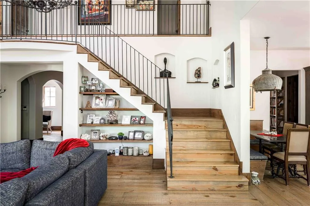 Hardwood staircase featuring wrought iron balusters and integrated shelving, complemented by hardwood flooring and arched entryways