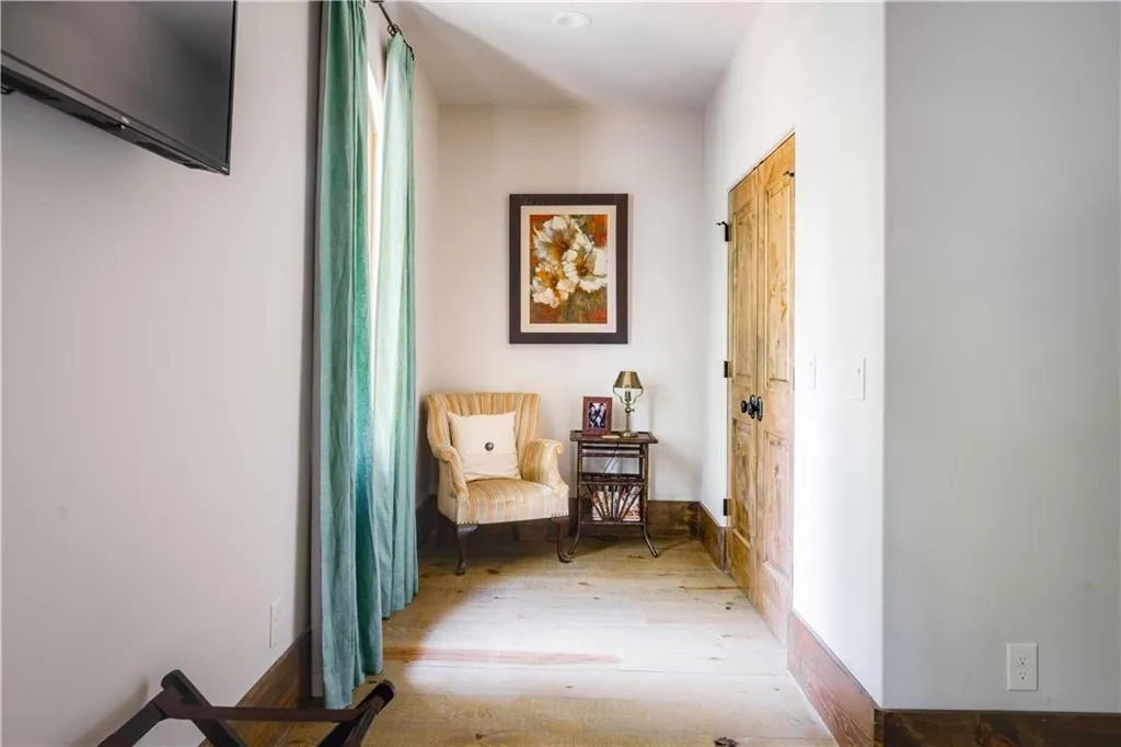 Hallway featuring wood-finish flooring, a rustic wood door with black hardware, and white baseboards