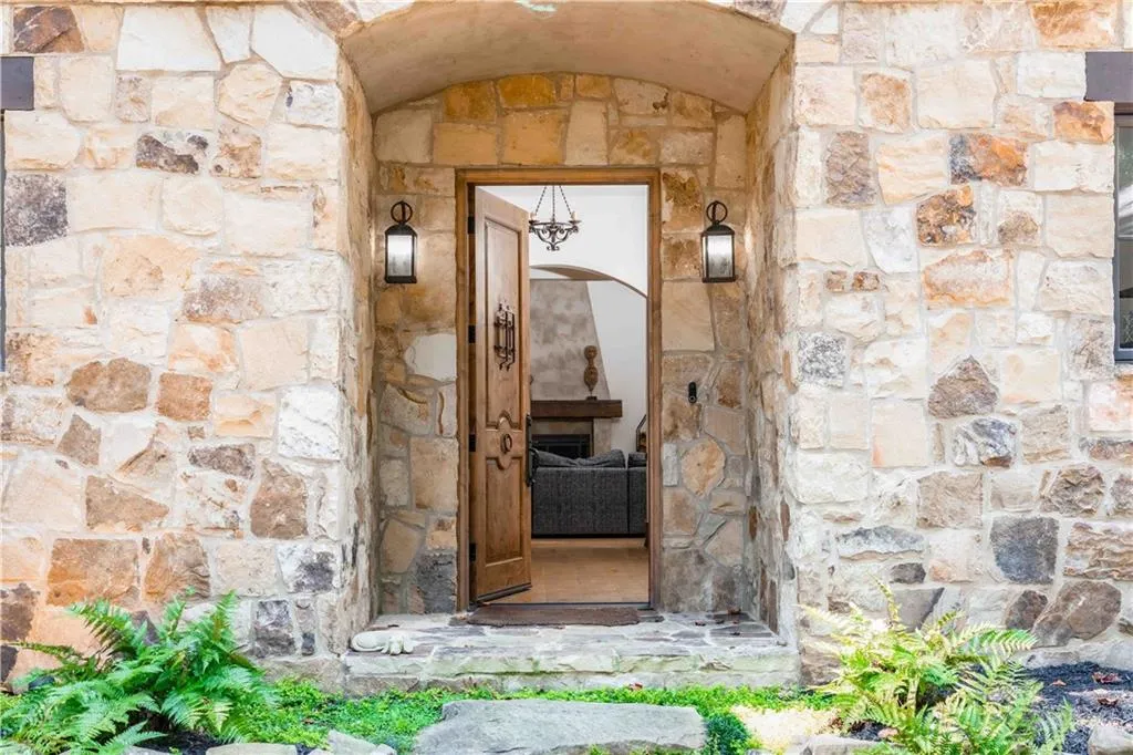 Stone facade entry with an arched doorway, wood door with decorative hardware, and two wall-mounted lanterns