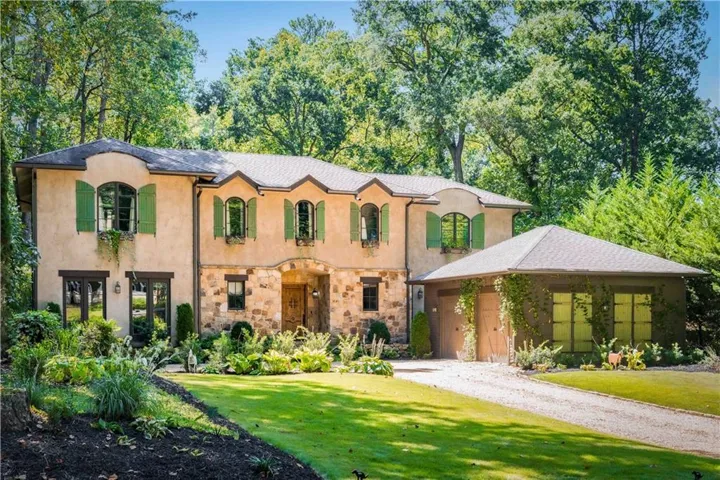 Stucco and stone exterior with arched entry, green louvered shutters, and window flower boxes