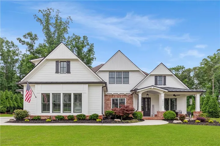 Contemporary farmhouse exterior featuring white siding, brick accents, a covered front porch, a metal roof accent, and a manicured lawn with mature landscaping