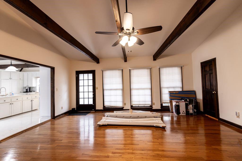 Unfurnished living room featuring dark hardwood / wood-style flooring, beam ceiling, and ceiling fan