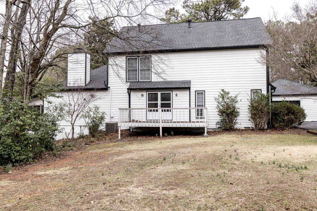 Back of property with central air condition unit, a wooden deck, and a lawn