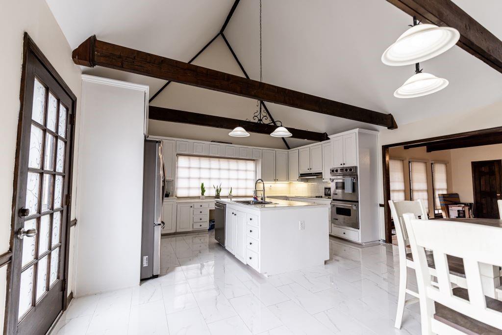 Kitchen featuring light tile flooring, an island with sink, pendant lighting, and beamed ceiling