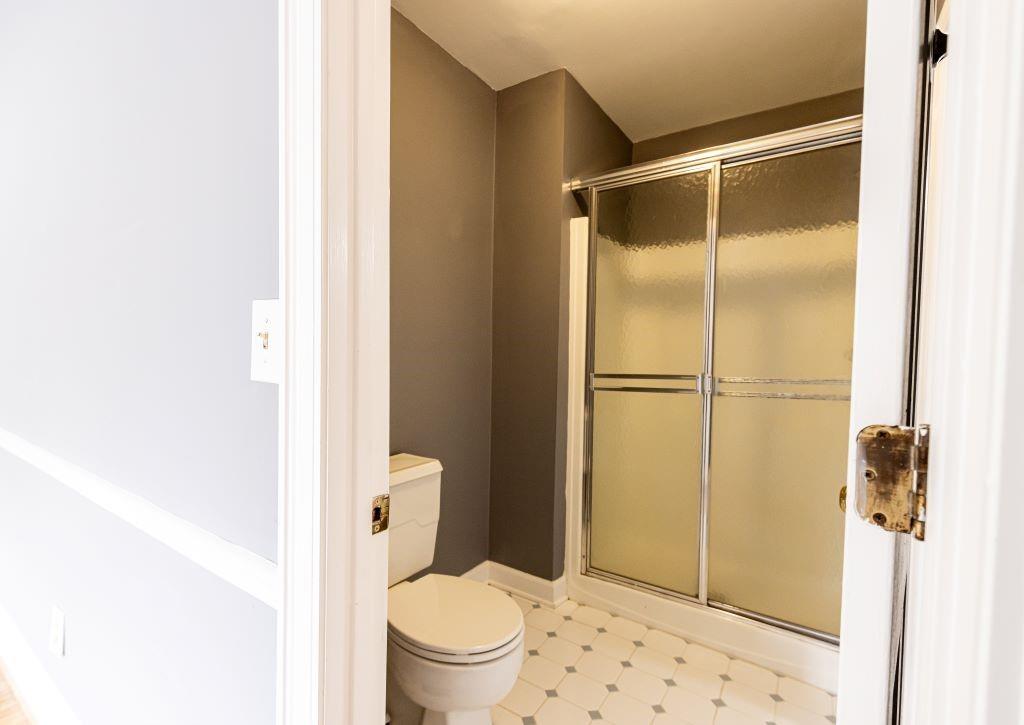 Bathroom featuring toilet, a shower with door, and tile floors