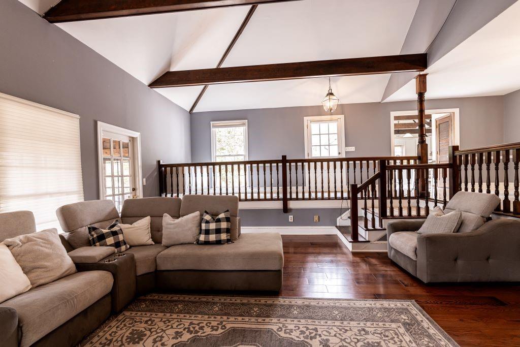 Living room with a notable chandelier, lofted ceiling with beams, and dark hardwood / wood-style flooring