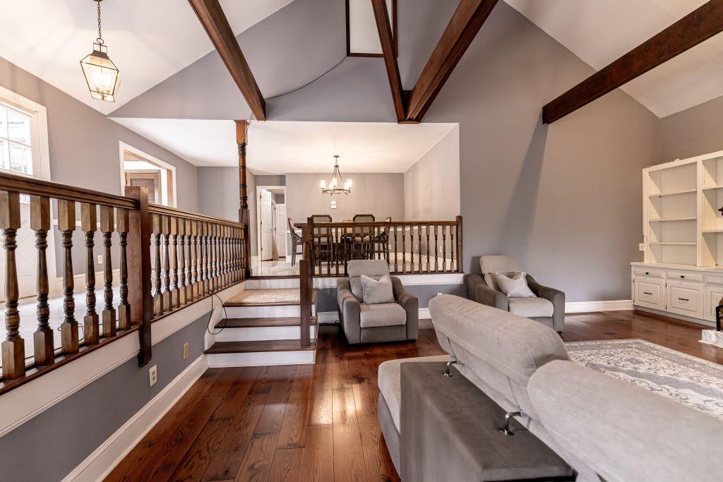 Living room with an inviting chandelier, high vaulted ceiling, beamed ceiling, and dark wood-type flooring