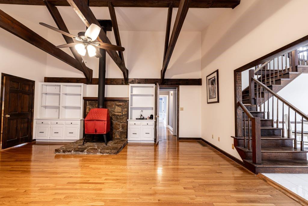 Unfurnished living room with light hardwood / wood-style flooring, beam ceiling, a wood stove, and ceiling fan