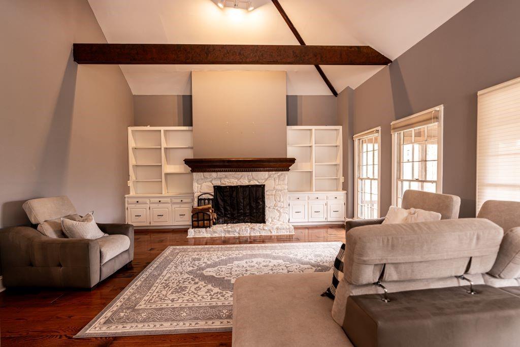 Living room featuring high vaulted ceiling, beamed ceiling, a stone fireplace, and dark wood-type flooring