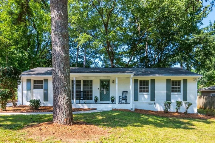 Single-story residence featuring a white painted brick exterior, dark green shutters, a welcoming front porch, and a dark shingle roof