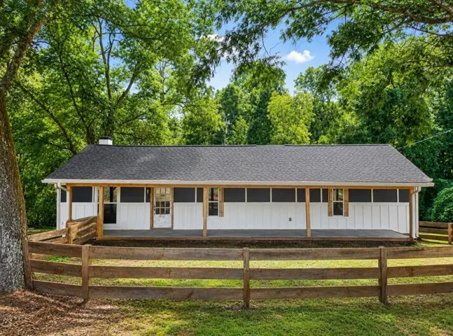Contemporary ranch-style residence featuring a dark shingle roof and a wooden fence