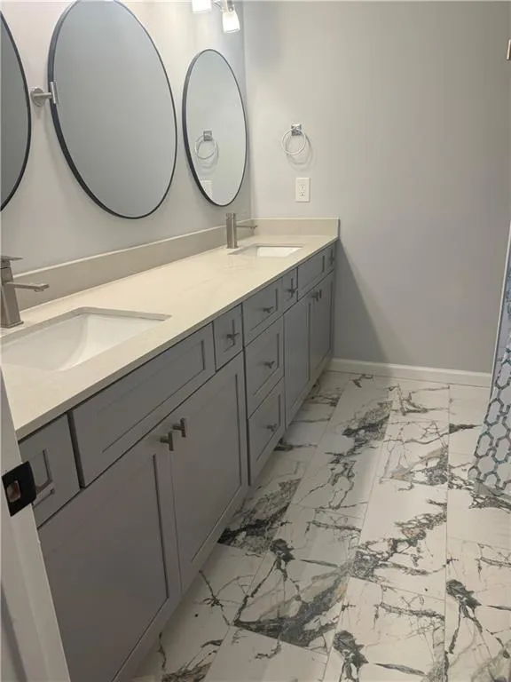 Full bath featuring double vanity and light marble finish flooring