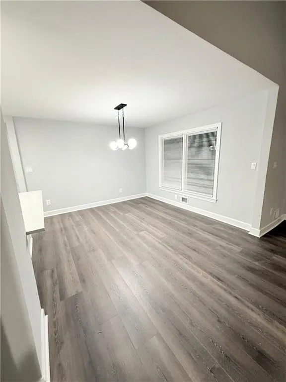 Unfurnished dining area featuring dark wood finished floors and a chandelier