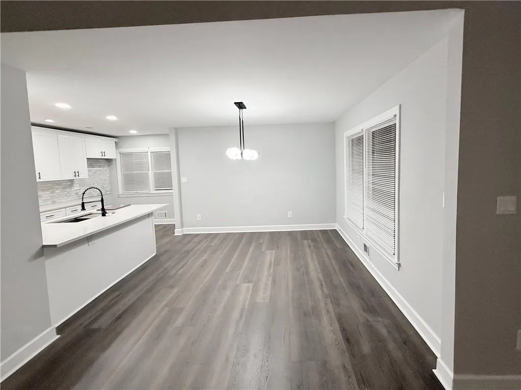 Kitchen with a chandelier, white cabinetry, dark wood-style floors, tasteful backsplash, and light stone counters