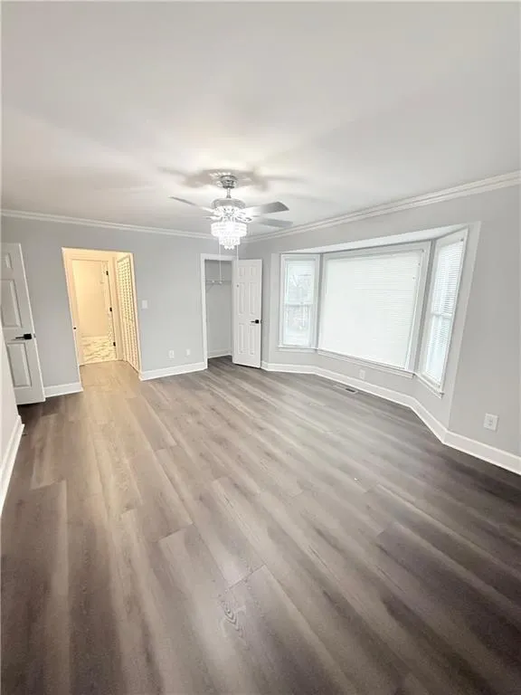 Unfurnished bedroom with crown molding, dark wood finished floors, a ceiling fan, and a spacious closet