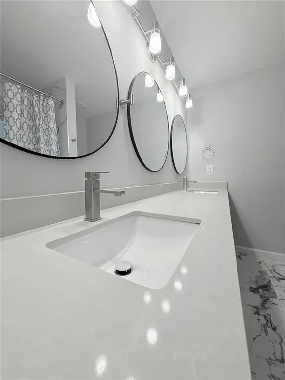 Full bathroom featuring double vanity, a shower with curtain, and marble look tile flooring