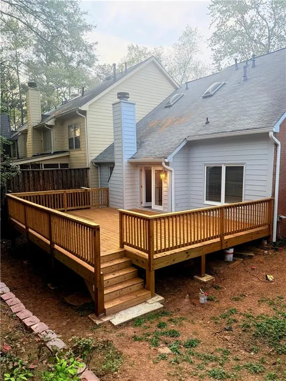 Rear view of property with a chimney, a deck, and roof with shingles