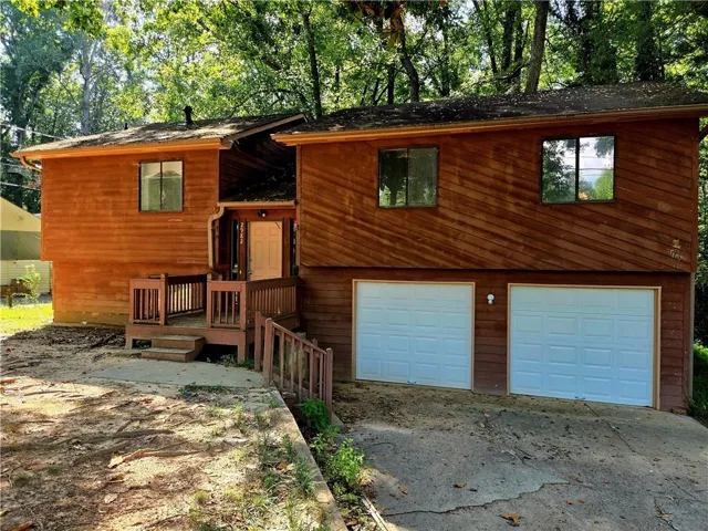 Wood-sided exterior with mature tree canopy, two-car garage, and an elevated entry with wood railing