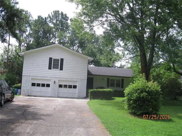 White siding exterior with a two-car garage, mature trees, manicured lawn, and a paved driveway