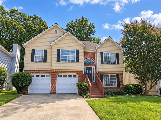 Multi-level residence featuring a brick and siding exterior, front entry porch, two-car garage, and established landscaping