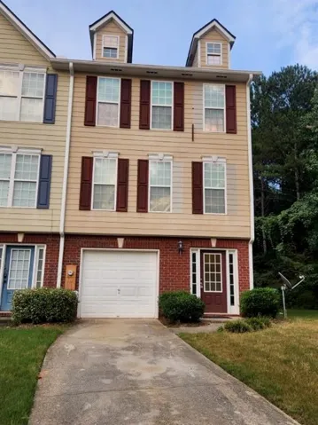 Three-story townhome with dormer windows, brick and siding exterior, attached garage, and a transom-style front door