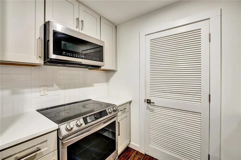 Kitchen featuring stainless steel appliances, dark wood finished floors, white cabinets, and decorative backsplash