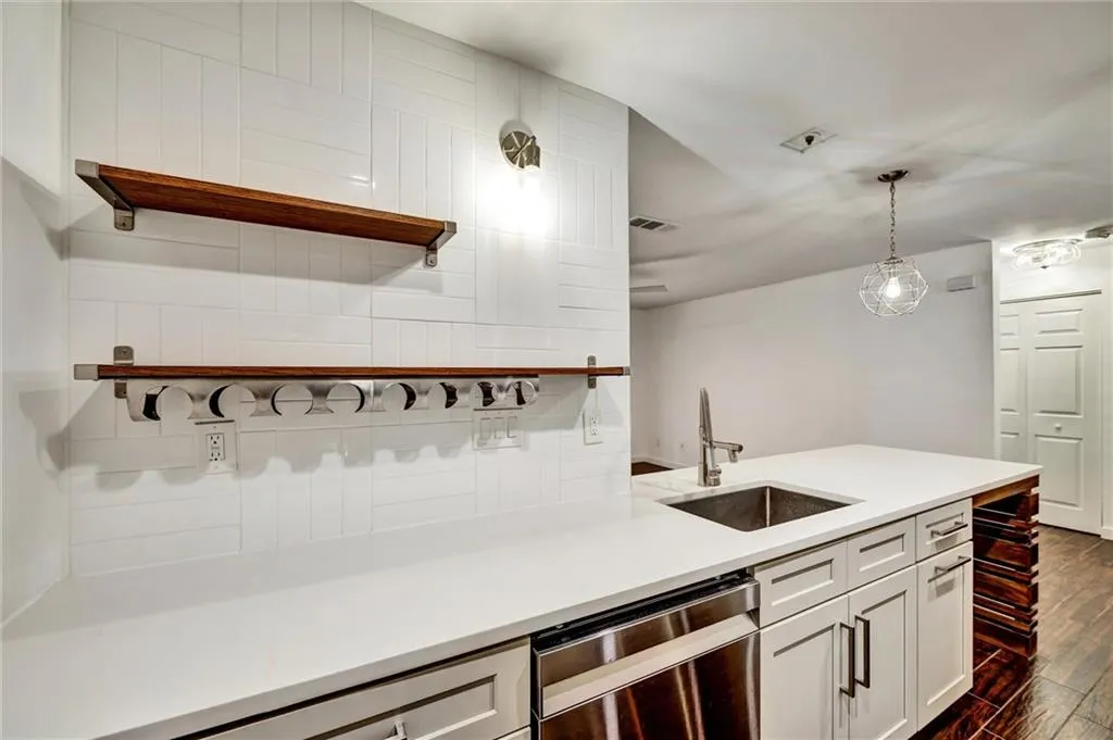 Kitchen with open shelves, dishwasher, white cabinetry, dark wood-style floors, and decorative light fixtures