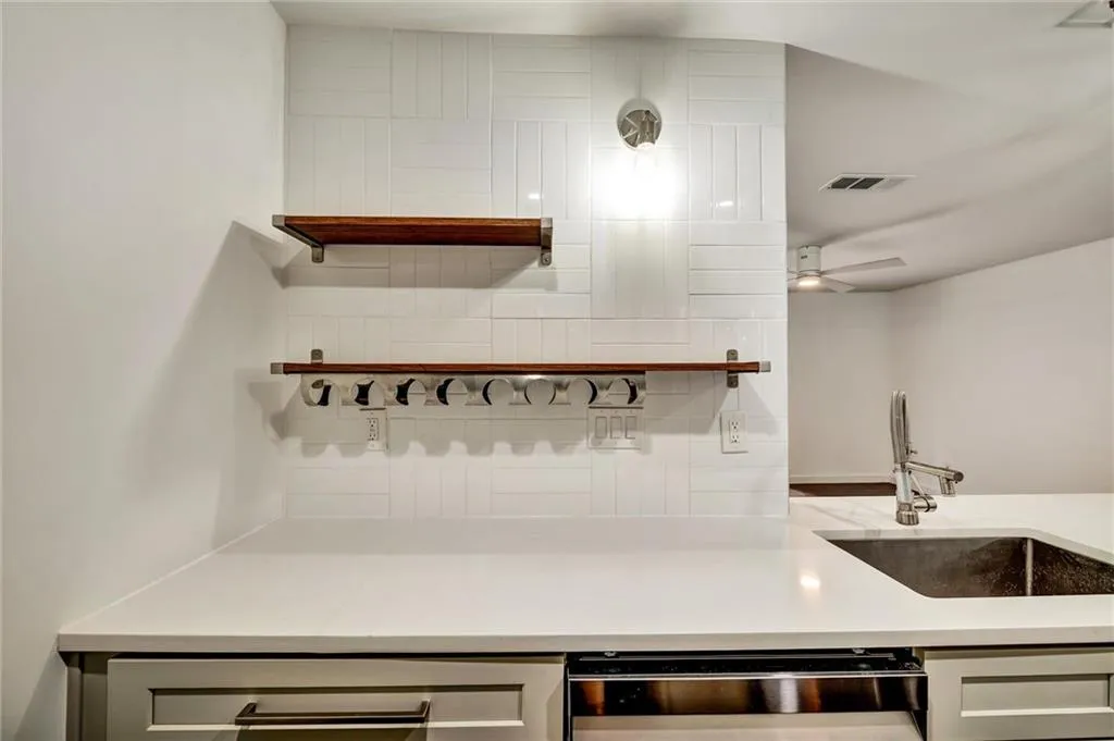 Kitchen with open shelves, dishwasher, decorative backsplash, and light stone countertops