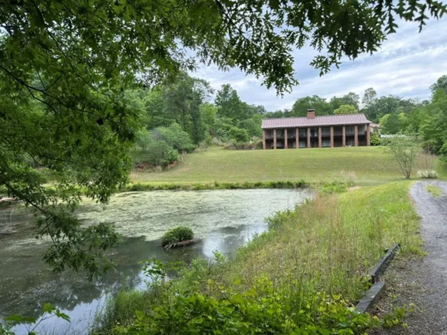 Expansive property featuring a large body of water, a gravel path, and a distant brick structure with a red roof and prominent chimney